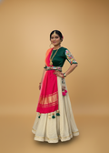 Woman wearing a traditional outfit with a green top, pink dupatta, and beige skirt on a beige background