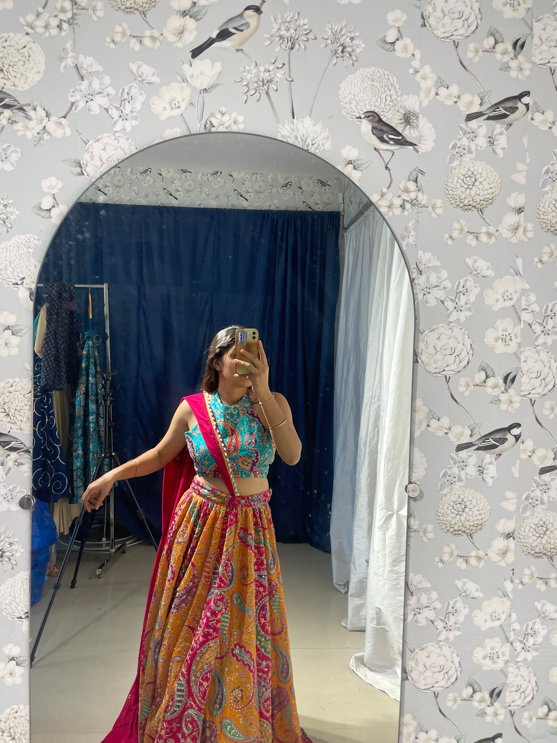 Woman in a colorful dress standing in front of a floral-patterned wall.